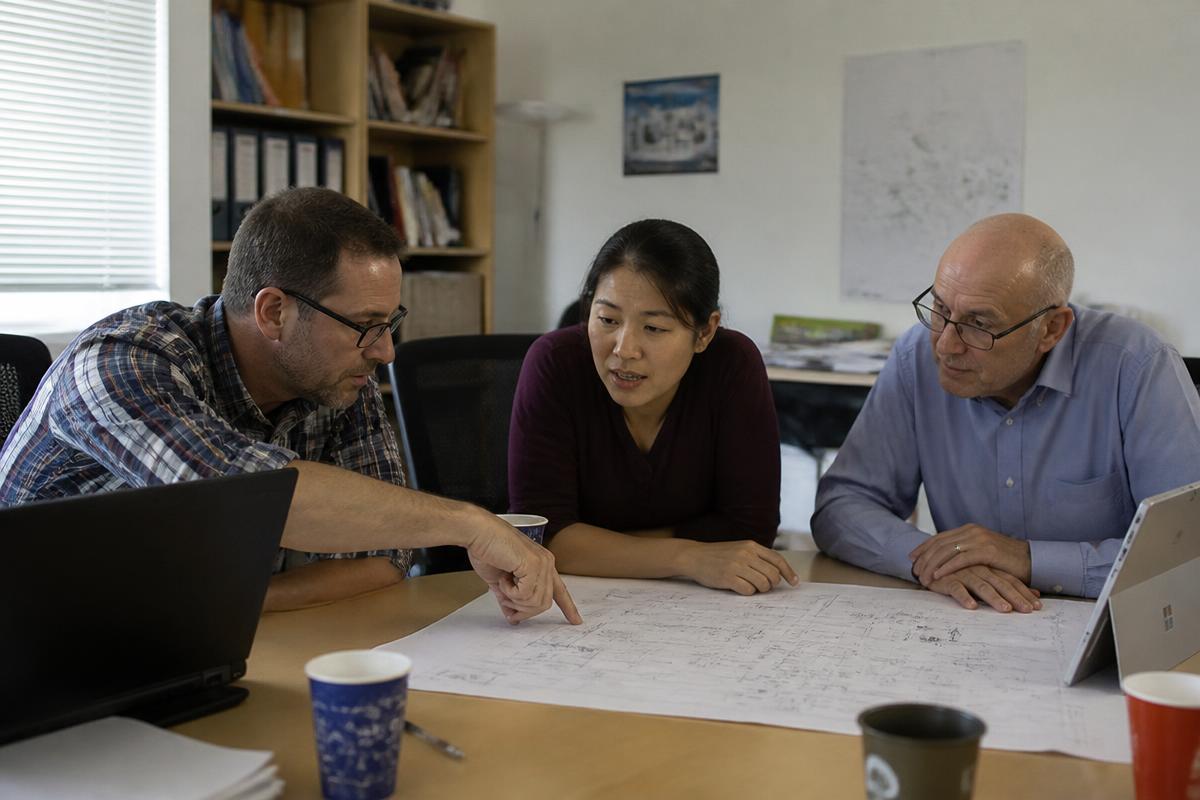 Three engineers discussing electrical drawings across a meeting table