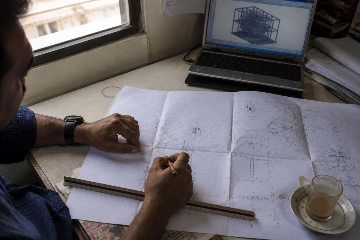 Engineer marking up a printed structural drawing beside a laptop showing a 3D model